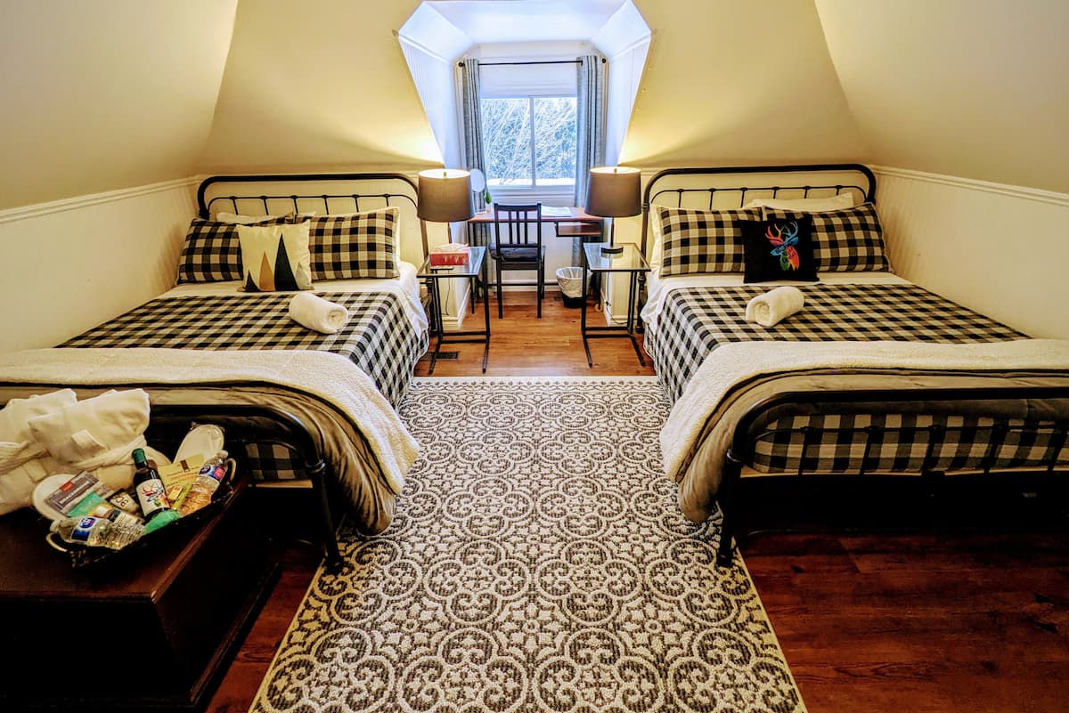 The Duke's Double Room at The Muskoka River Chalet with two iron-frame beds in buffalo check bedding, dormer window with snowy Muskoka view