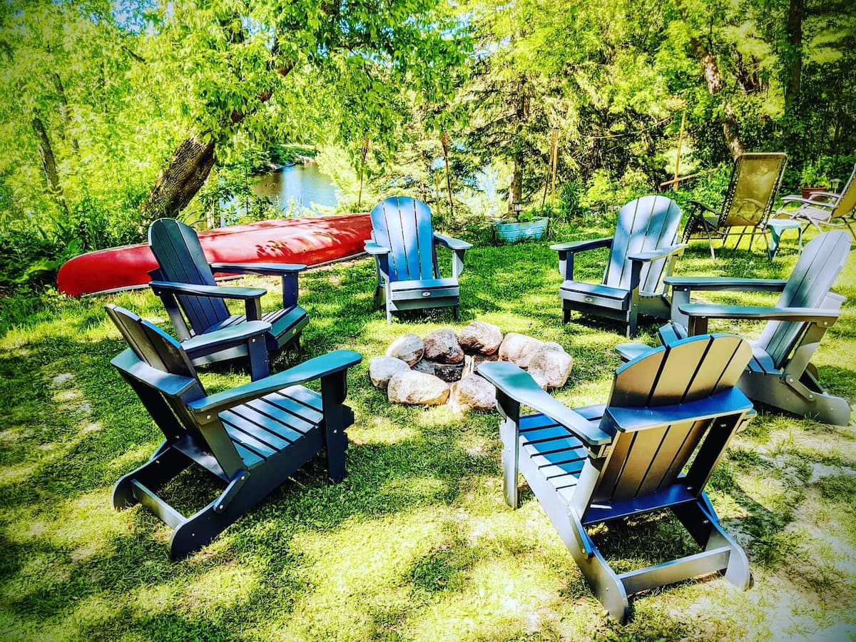 Stone fire pit with Muskoka chairs and red canoe on the Muskoka River at The Muskoka River Chalet