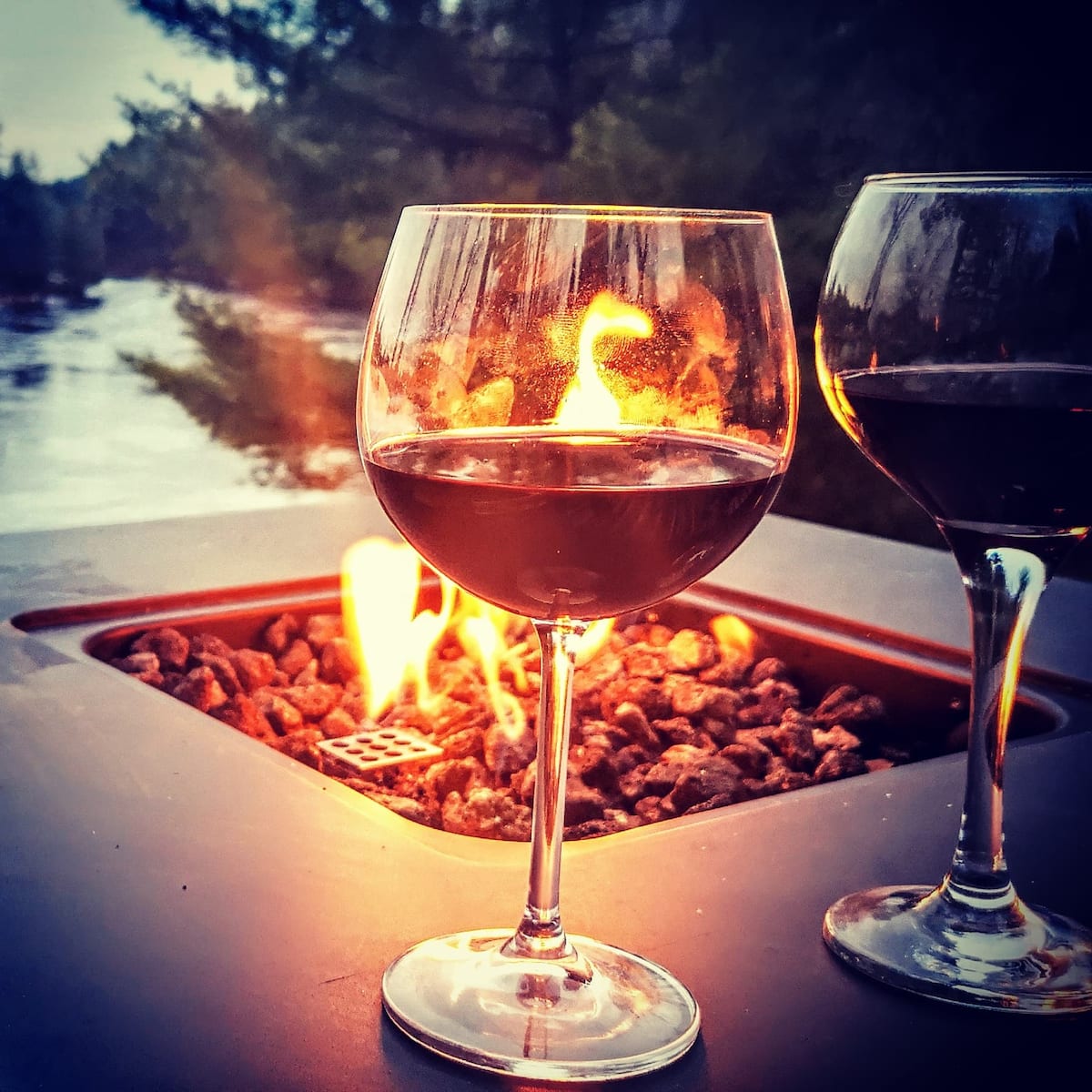 Wine glasses by the fire pit at dusk overlooking the Muskoka River