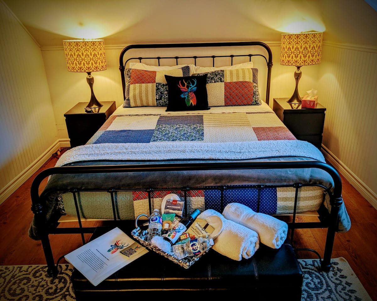 The Royal River View Room at The Muskoka River Chalet with an iron-frame bed, patchwork quilt, and warm ambient lighting